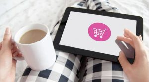 A woman shopping online using her tablet while holding a cup of coffee