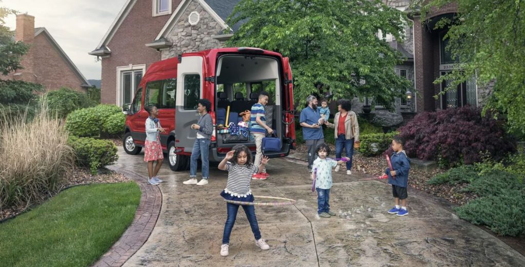 A large family preparing to depart on a trip in their red 2021 Ford Transit Connect Van in San Antonio, TX